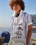 Boy at beach wears a blue-and-white long-sleeve shirt over a white Polo 67 shirt.