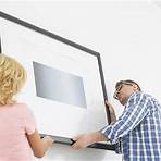 Man and woman hanging a framed piece on a wall
